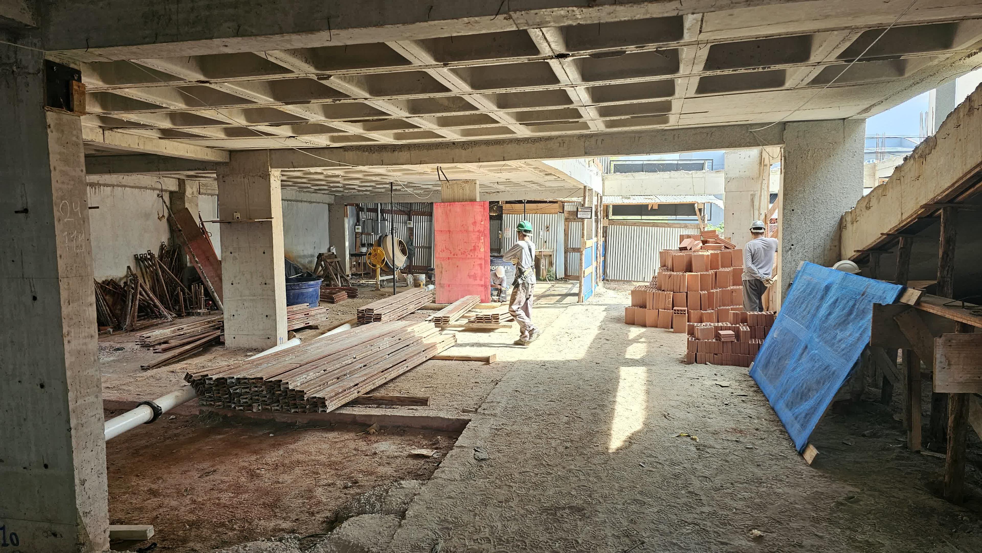 Canteiro de obras ativo com estoque de blocos de alvenaria e operários